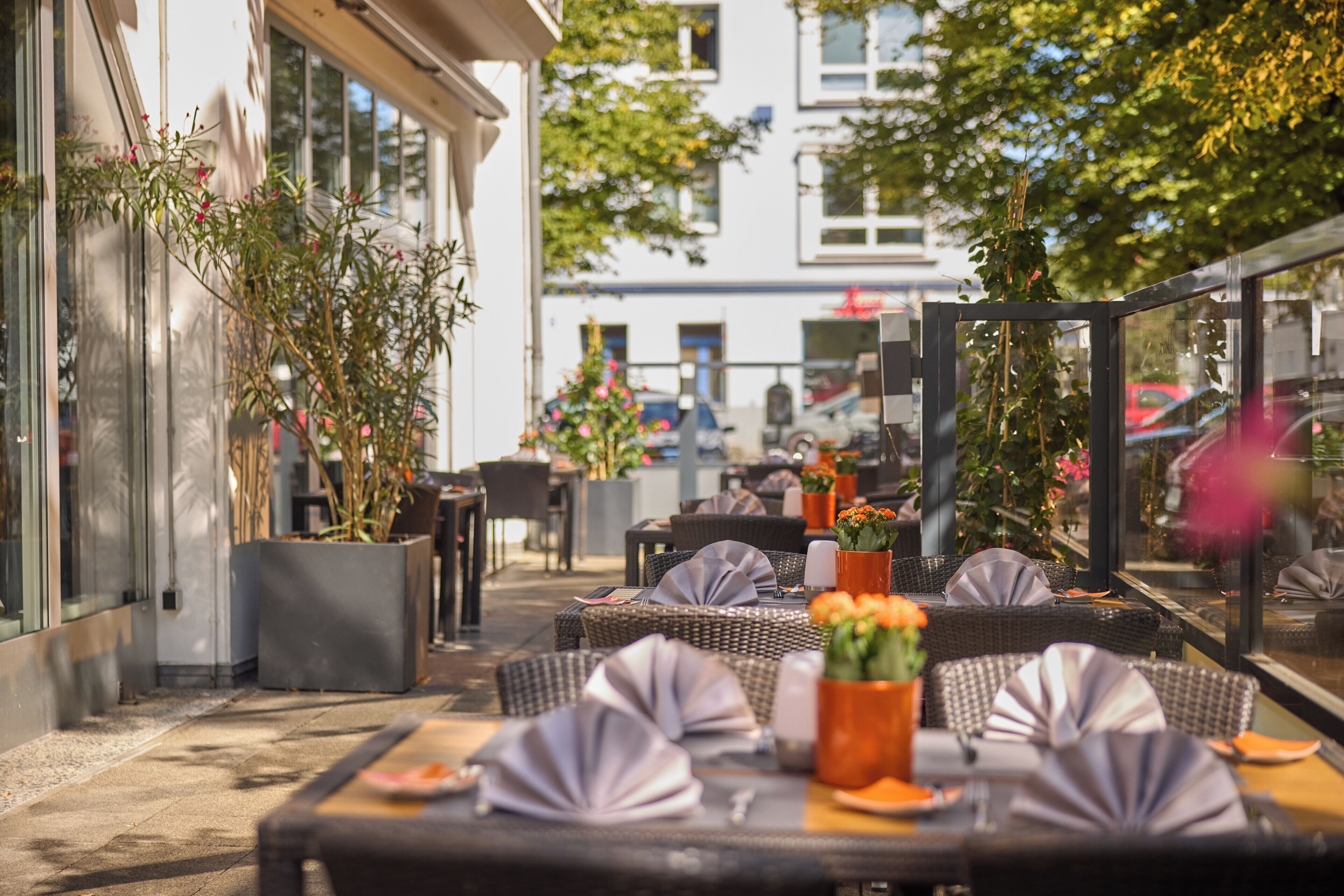 Ein Sitzbereich im Freien mit Tischen und Stühlen, Blumentöpfen und Blick auf die Straße.
