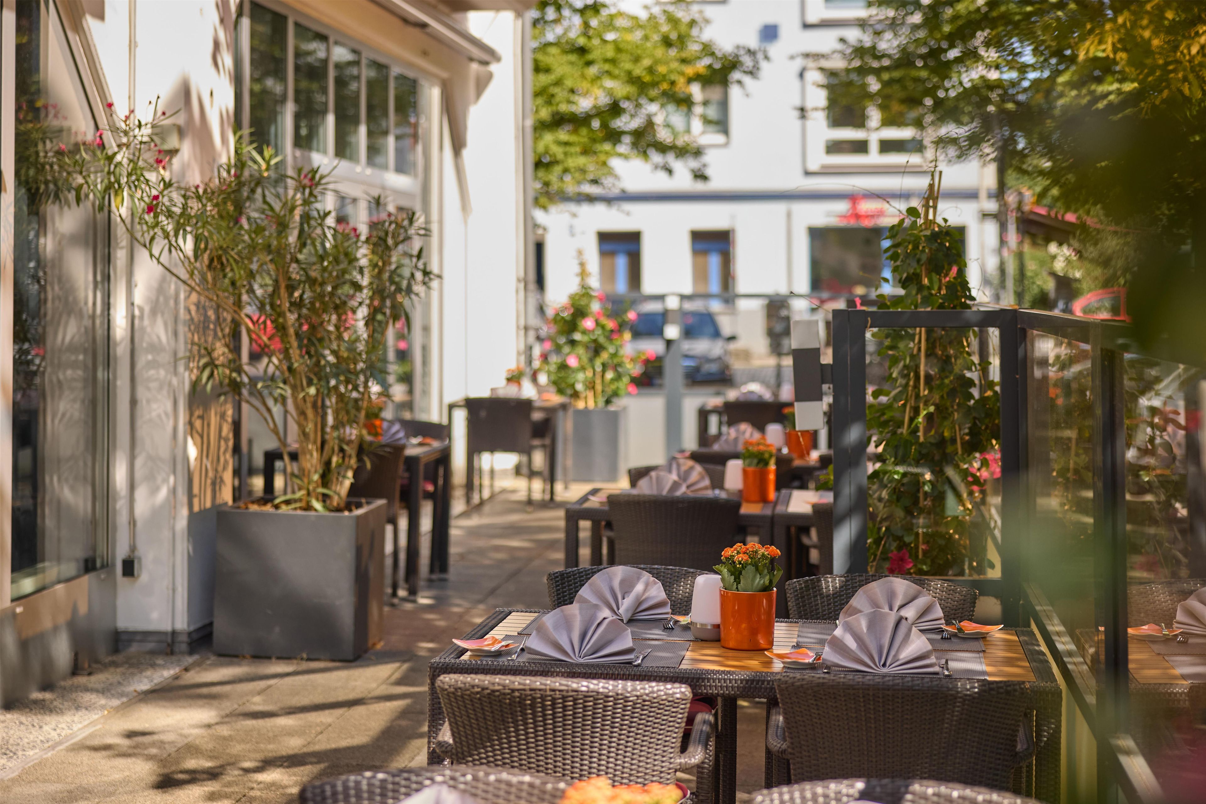 Un café en plein air avec des meubles en osier, des plantes en pot et une vue sur la rue.