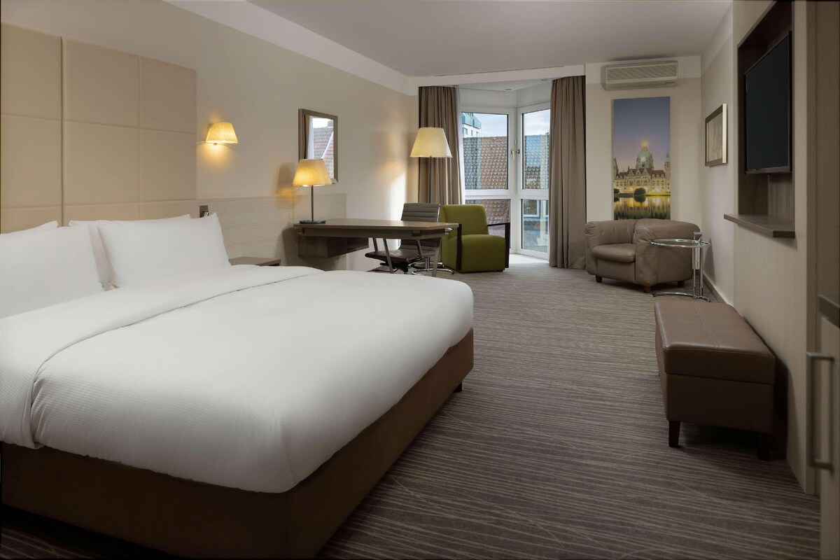 Una habitación de hotel con una cama grande, un escritorio con silla, un sofá y un televisor.