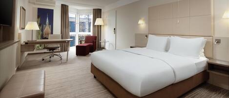 A hotel room with a large bed, a desk with a chair, a small table, and a TV mounted on the wall.