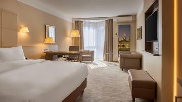 A hotel room with a large bed, a desk with a chair, a small sofa, and a TV mounted on the wall.