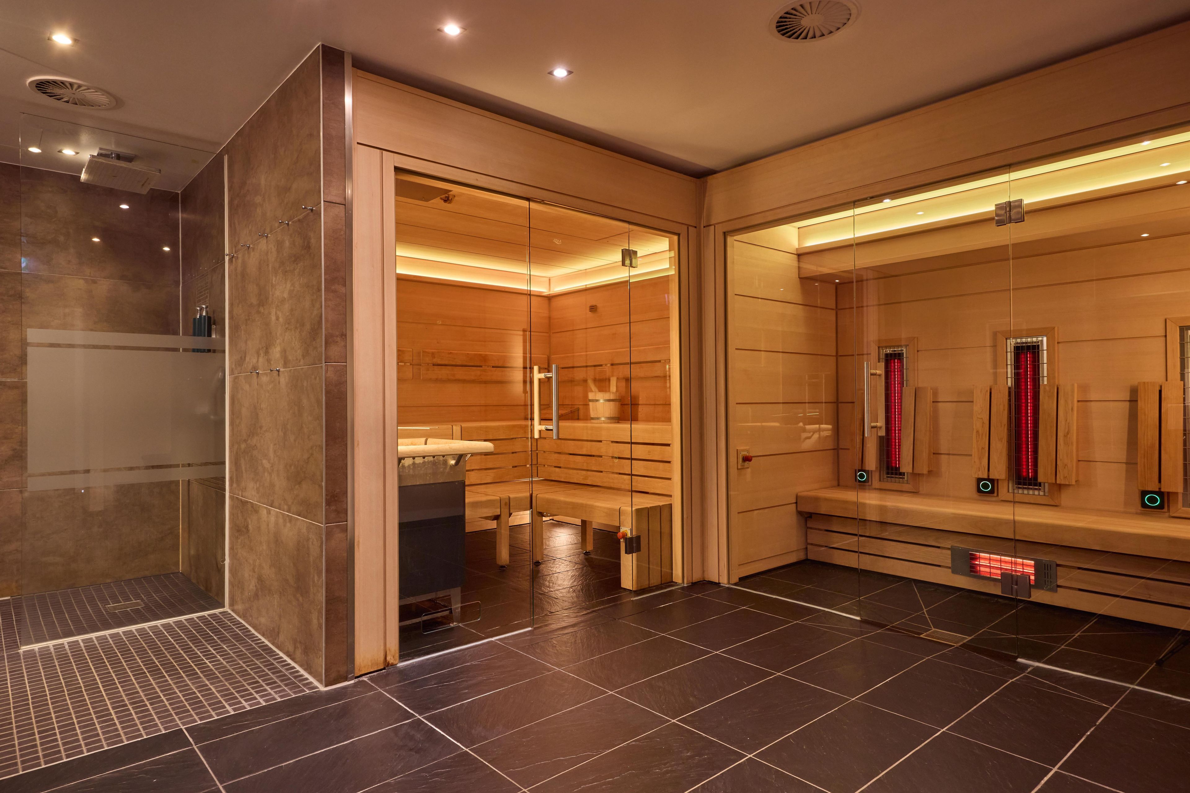 Une salle de bain moderne dotée d’un sauna en verre, d’une zone de douche séparée et d’un banc pour se détendre.