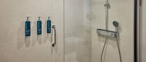 A modern bathroom with a glass shower enclosure, a handheld showerhead, and three bottles of Crabtree body wash.