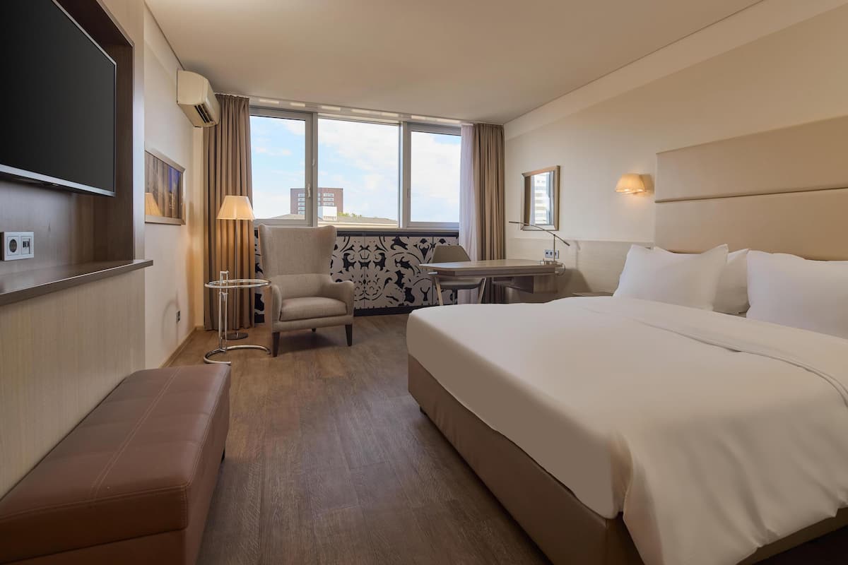 A hotel room with a large bed, a desk, a chair, a TV, and a window with curtains.