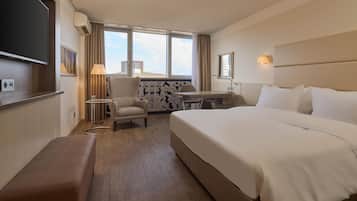 A hotel room with a large bed, a desk, a chair, a TV, and a window with curtains.