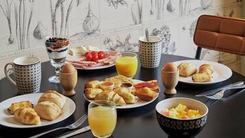 A breakfast table with plates of croissants, pastries, and fruit, along with glasses of orange juice and a coffee cup.