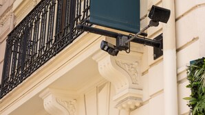 Fachada de edificio con detalles arquitectónicos ornamentales y un letrero colgante con un logotipo estilizado.
