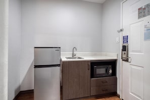 A compact kitchen with a refrigerator, sink, microwave, and wooden cabinets.