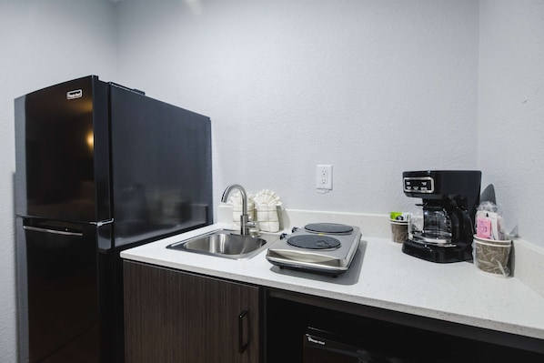 A compact kitchen with a black refrigerator, a sink, a coffee maker, and a small countertop area.