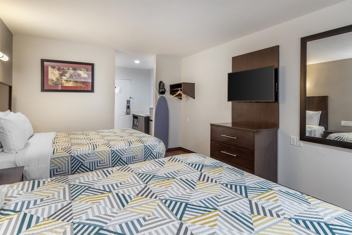 A hotel room with two beds, a television, a dresser, and a mirror.