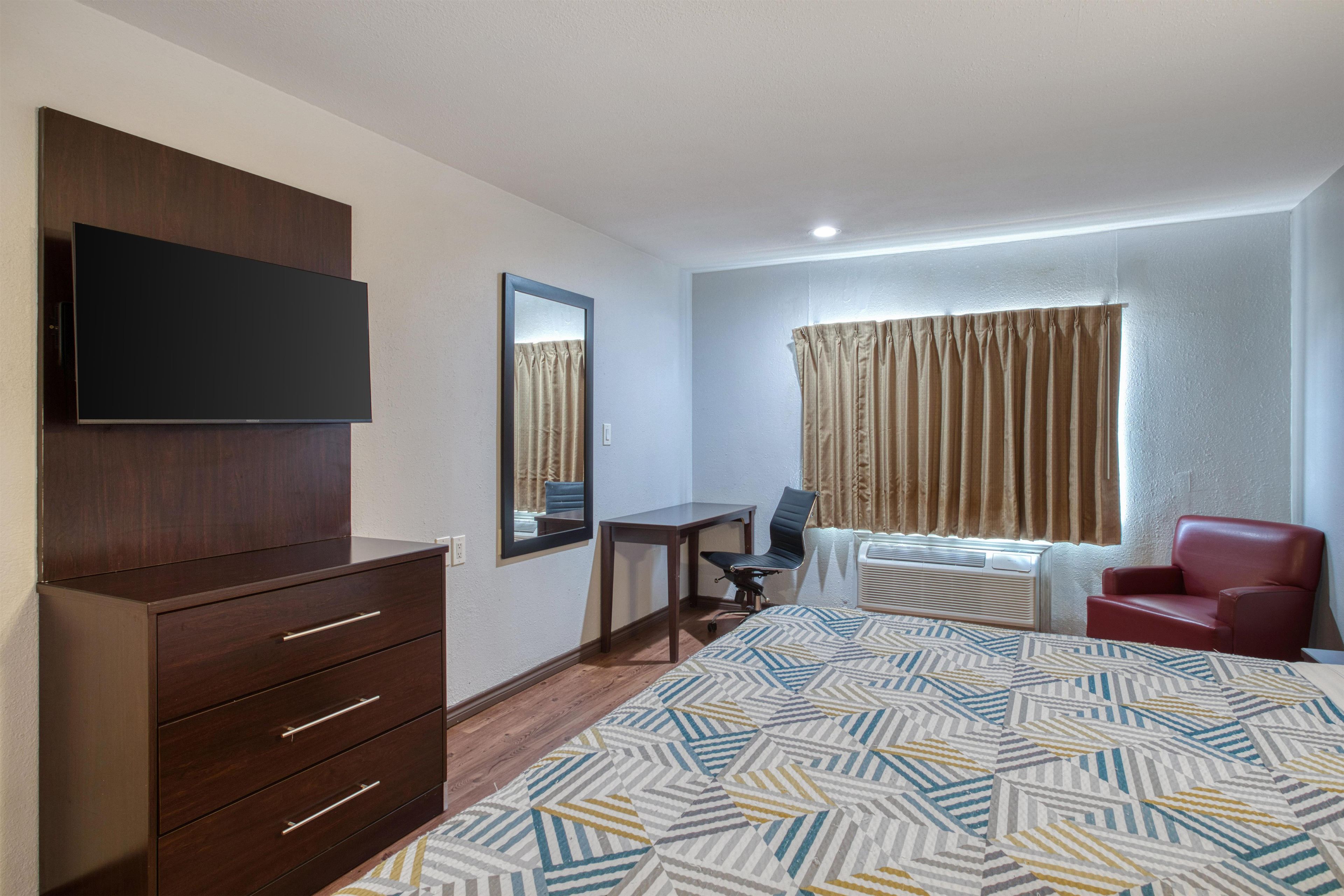 A hotel room with a bed, a desk, a chair, a television, and a window with curtains.