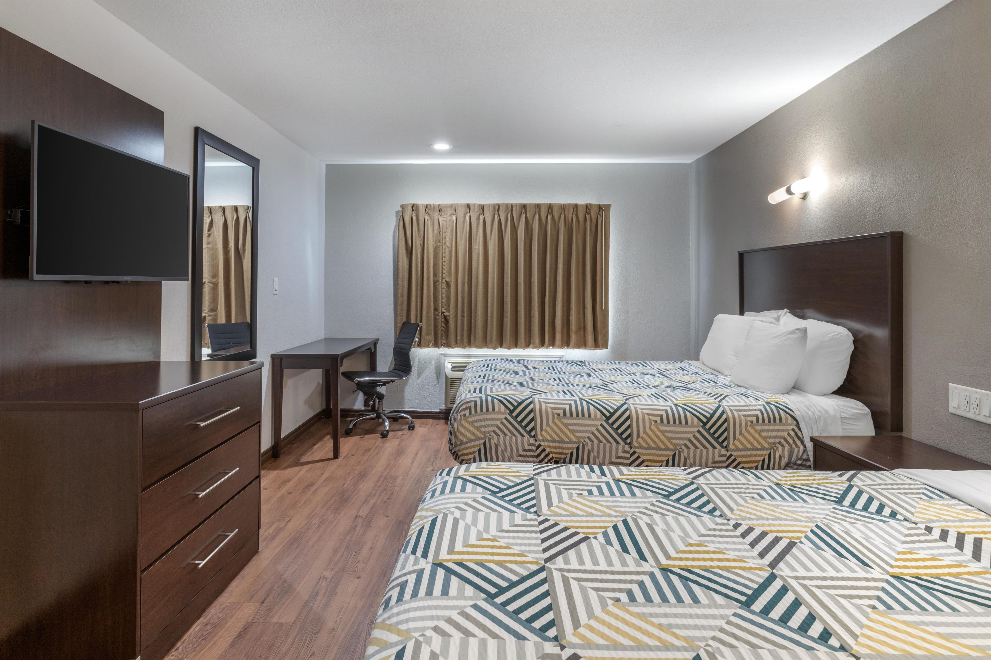 A hotel room with a large bed, a desk, a chair, a television, and a window with curtains.
