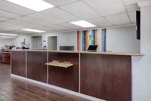 A reception desk with a flat-screen monitor, a laptop, and a small shelf.