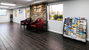A hotel lobby with dark wood flooring, a stone accent wall, red leather chairs, a table, and a display rack with brochures. - SureStay by Best Western Channelview Houston East (Channelview)