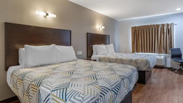 A hotel room with two beds, a desk, and a window with curtains.