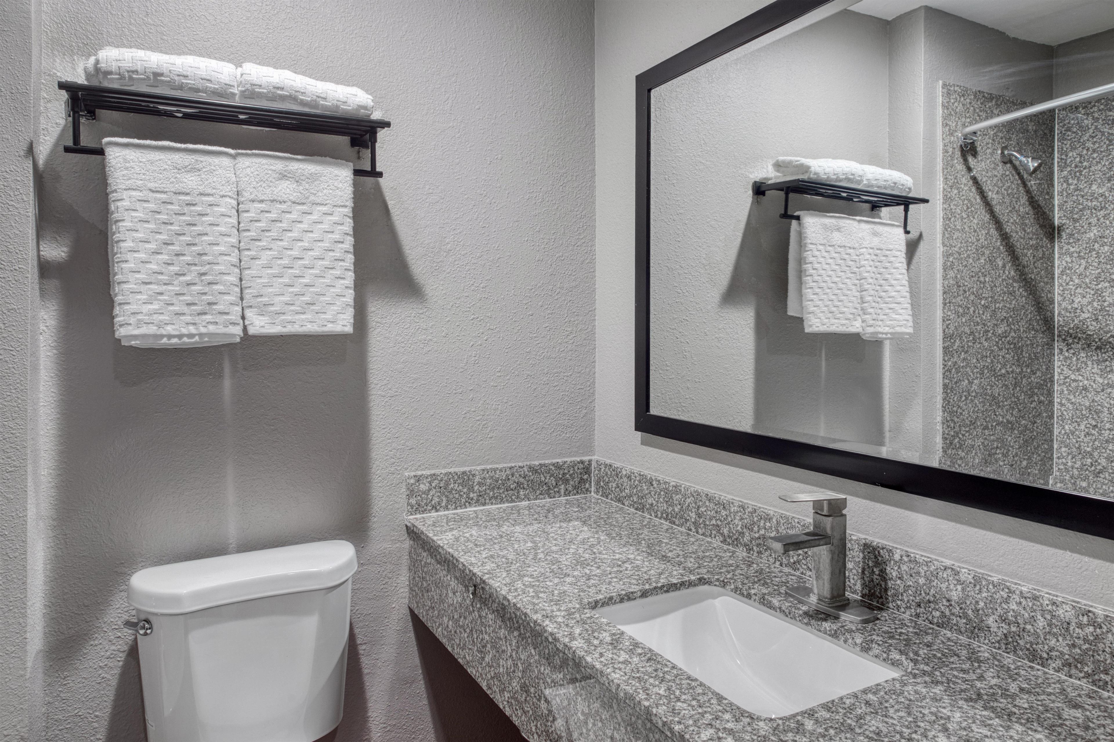 Un baño con inodoro, lavamanos, espejo y dos toallas colgadas en un perchero.