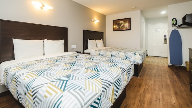 A hotel room with two beds, a wooden floor, a door, and a wall-mounted shelf. - SureStay by Best Western Channelview Houston East (Channelview)