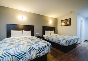 Habitación de hotel con dos camas, una mesita de noche, una lámpara de pared y un cuadro enmarcado.