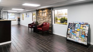 A reception area with a stone wall, a bulletin board with brochures, and a seating area with chairs and a table. - SureStay by Best Western Channelview Houston East (Channelview)