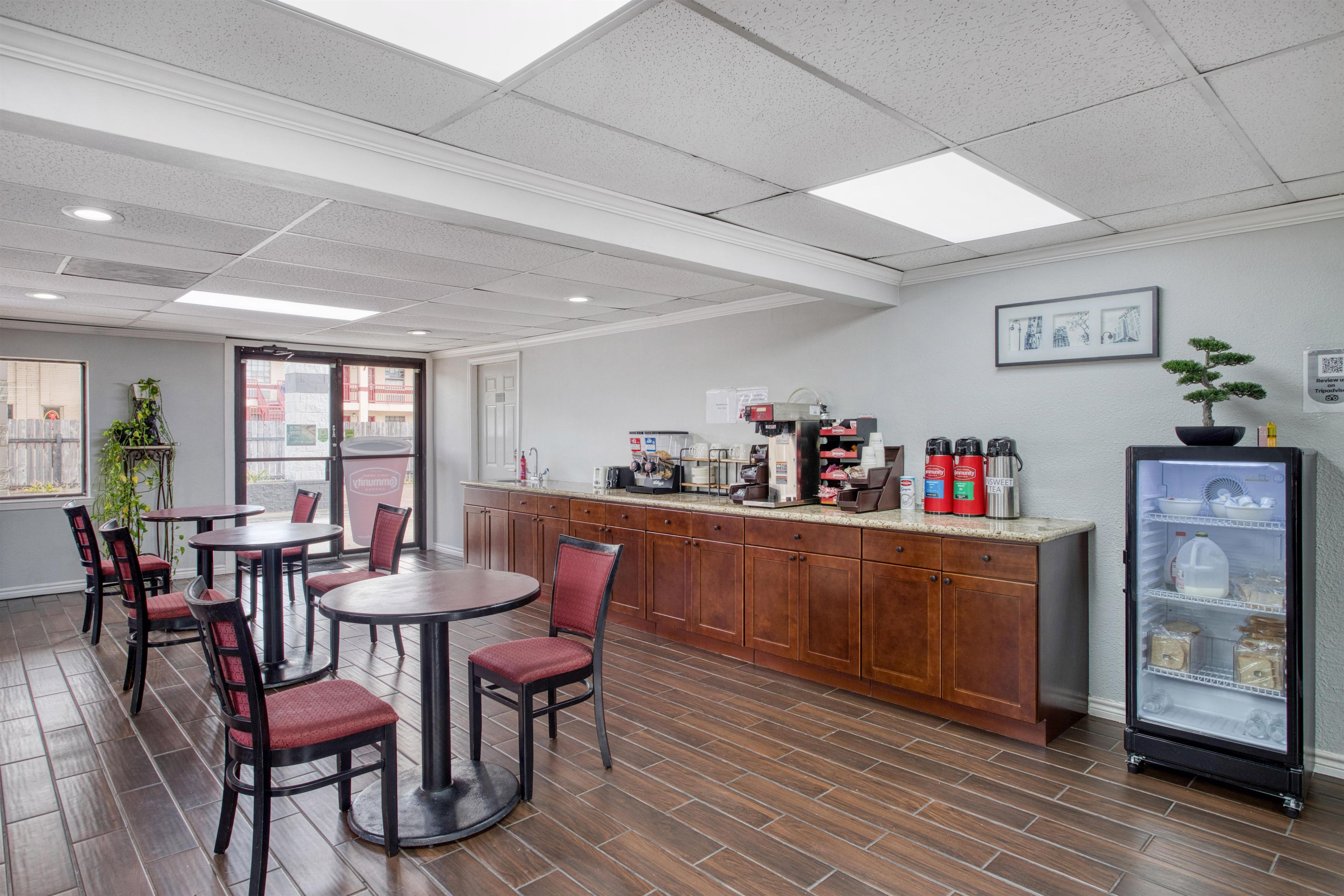 Una cafetería con piso de madera, una barra con máquinas de café y un refrigerador con bebidas.