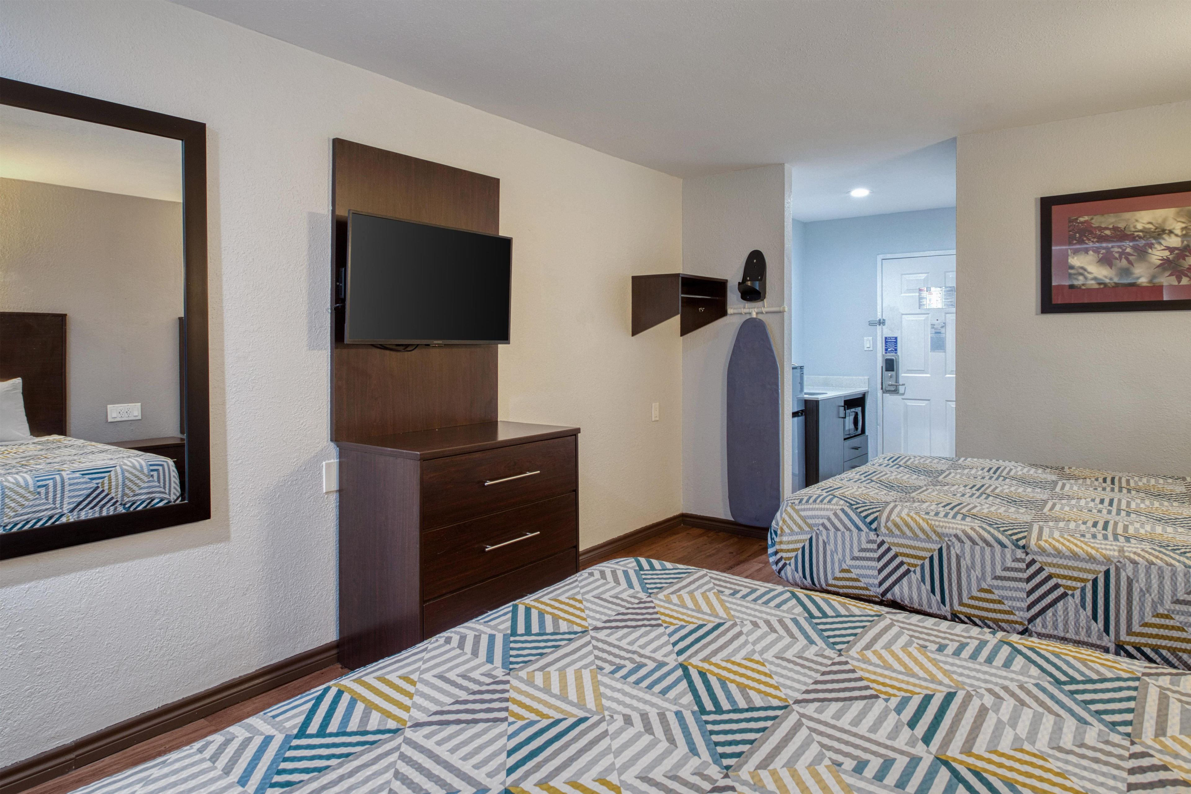 A hotel room with a bed, a dresser, a television, and a bathroom visible through an open door.