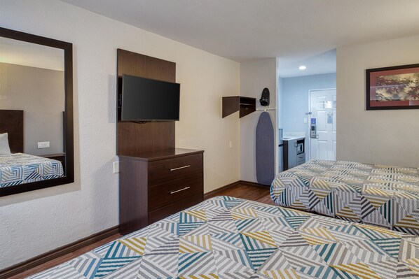 A hotel room with a bed, a dresser, a television, and a bathroom visible through an open door.