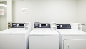 A laundry area with three white washing machines, a sign indicating laundry for registered hotel guests only, and a no-smoking sign. - SureStay by Best Western Channelview Houston East (Channelview)