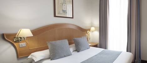 A hotel room with a large bed, two bedside lamps, a nightstand, a framed picture on the wall, and a window with curtains.
