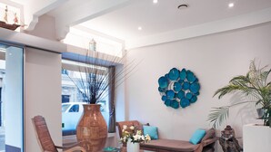 A modern living room with a glass coffee table, wooden rocking chair, and a sofa with blue cushions. - Hôtel Esprit d'Azur (Nice)