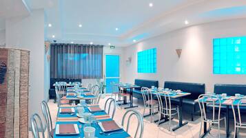 A modern dining area with multiple tables and chairs, a blue accent wall, and a large window with a view.