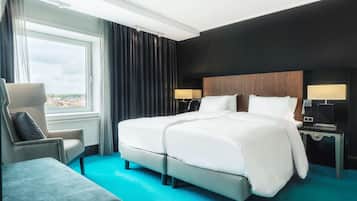 A hotel room with a large bed, a chair, a nightstand, and a view of the city.