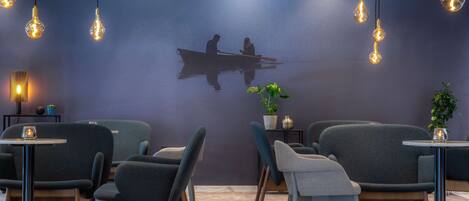 A modern interior with seating and tables, a wall mural, and hanging light fixtures.