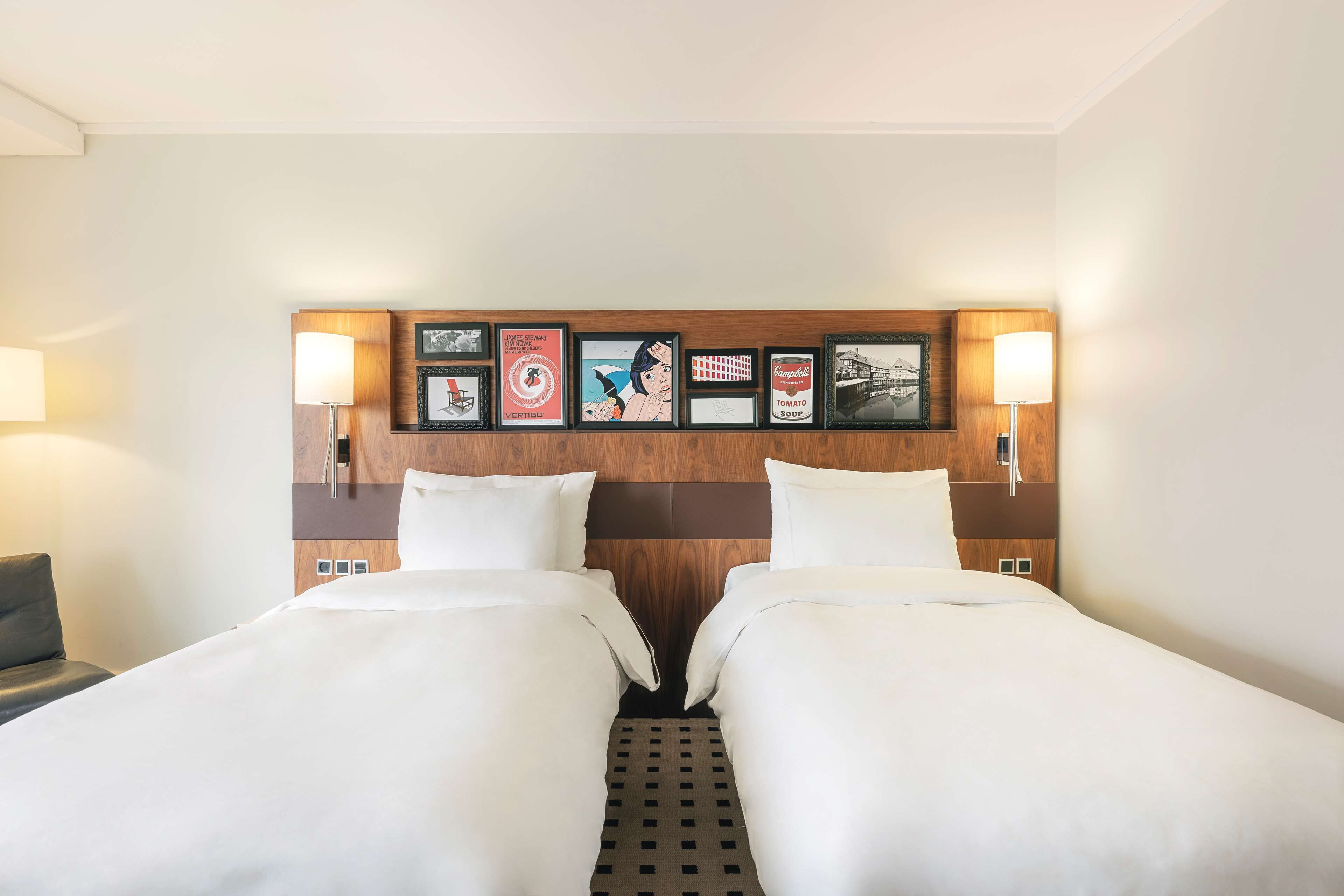 A hotel room with two beds, a wooden headboard, framed pictures, and bedside lamps.