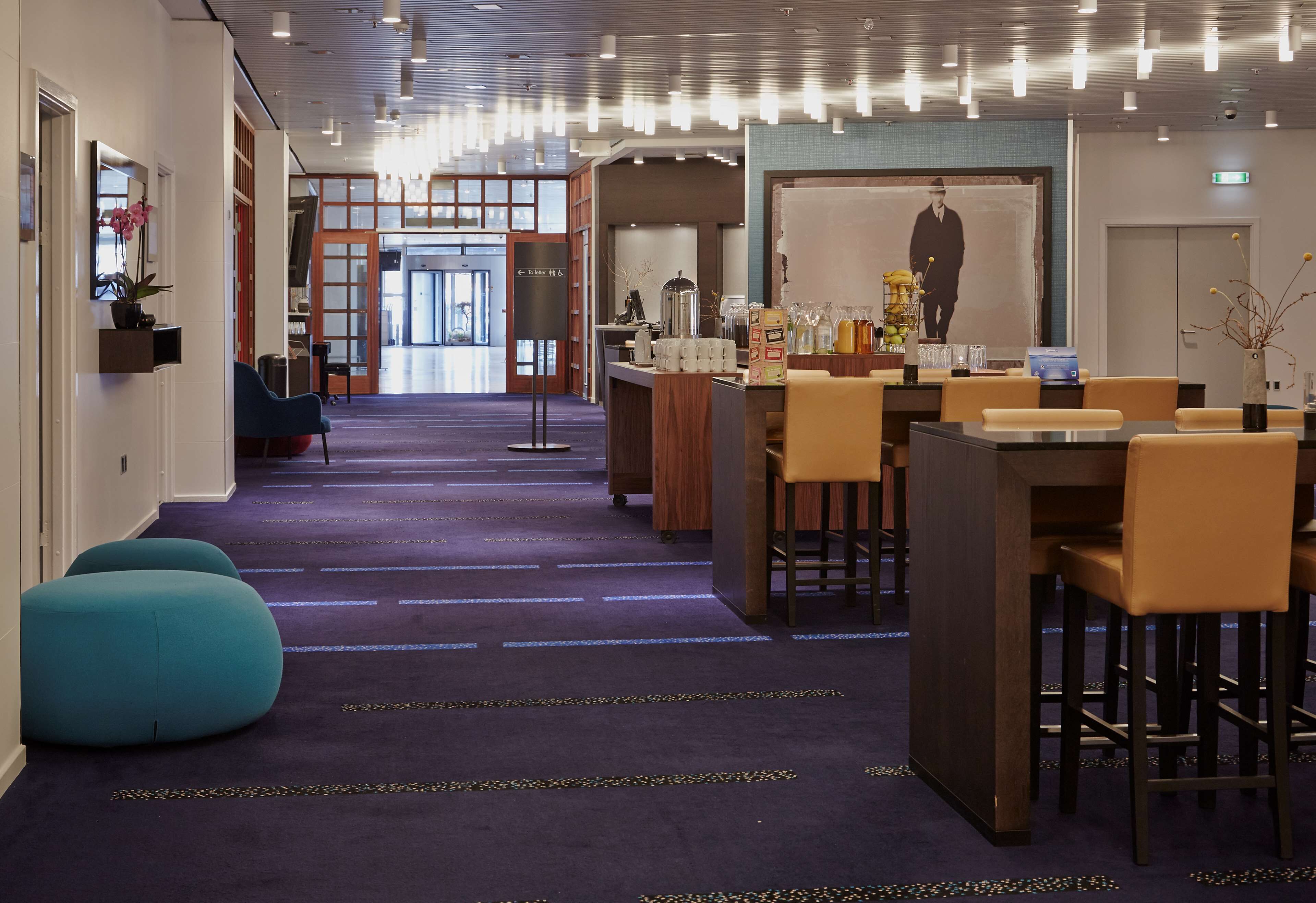 A hotel lobby with a reception desk, seating area, and a large poster on the wall.
