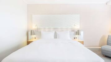 Una habitació d'hotel amb un llit gran, dues taules de nit amb làmpades, un capçal de llit amb disseny texturat i un armari solitari gris.