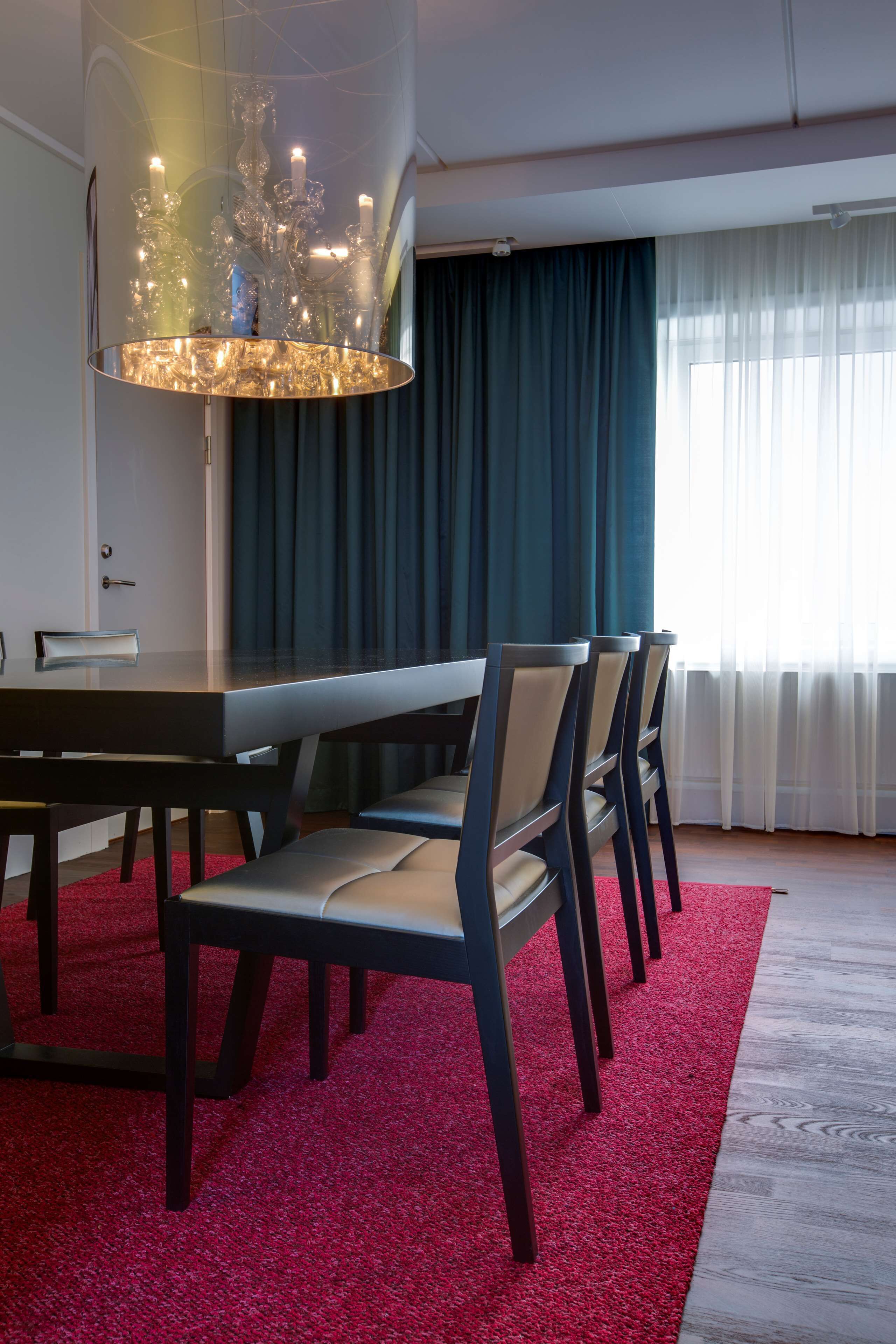 Un comedor con una mesa y sillas modernas, una araña y vistas al exterior a través de cortinas translúcidas.