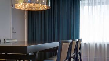Un comedor con una mesa y sillas modernas, una araña y vistas al exterior a través de cortinas translúcidas.