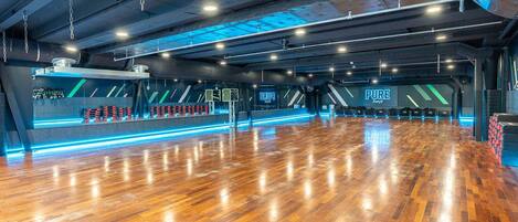 A spacious dance studio with a polished wooden floor, mirrored walls, and blue LED lighting.