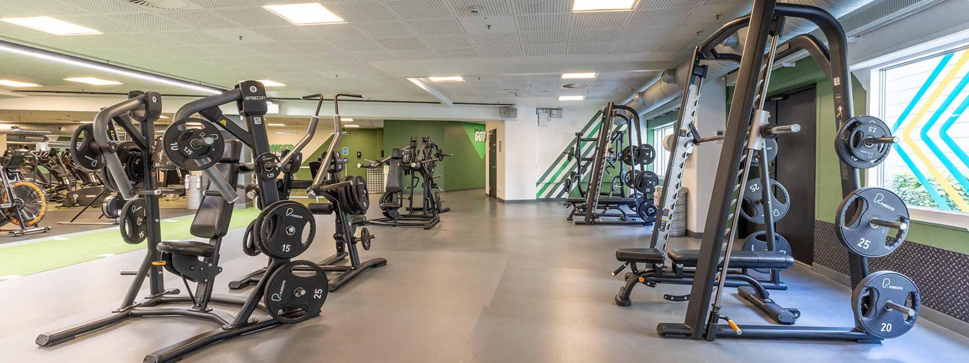 A gym with various weightlifting equipment, including benches and squat racks, arranged in a spacious layout.