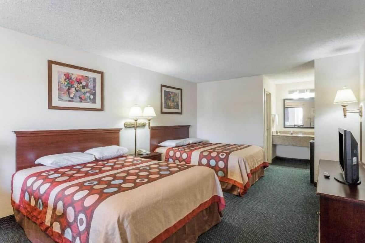 A hotel room with two beds, a desk, a television, and a bathroom visible in the background.