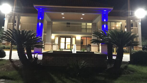 A hotel entrance with a covered entrance, illuminated blue lights, and two palm trees in the foreground. - Super 8 by Wyndham Slidell (Slidell)