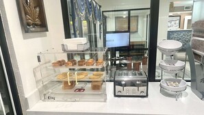 A breakfast station with a glass display case containing muffins and waffles, a toaster, and a coffee maker. - Super 8 by Wyndham Slidell (Slidell)