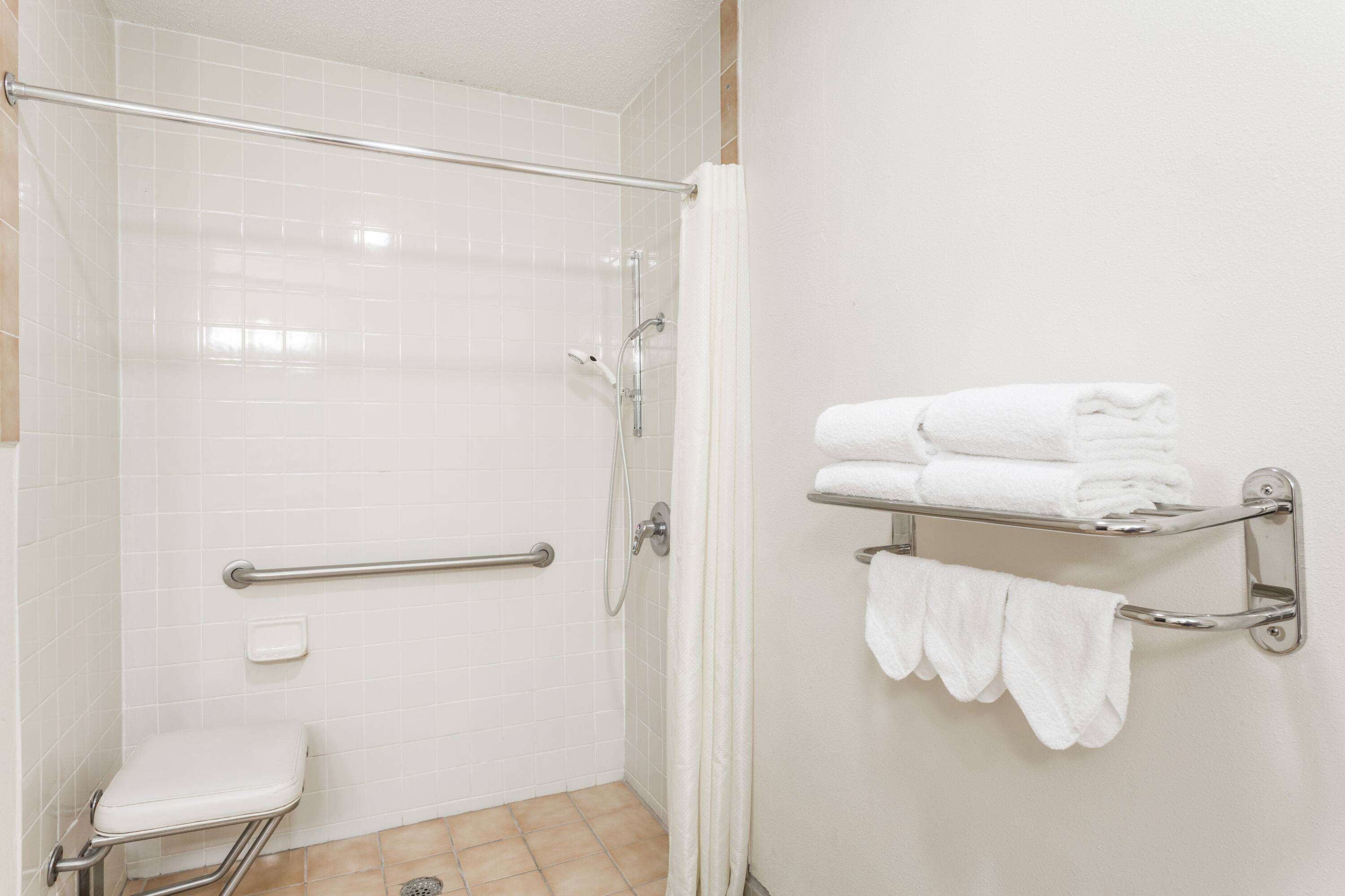 A bathroom with a white toilet, a shower with a grab bar, and a towel rack with folded towels.