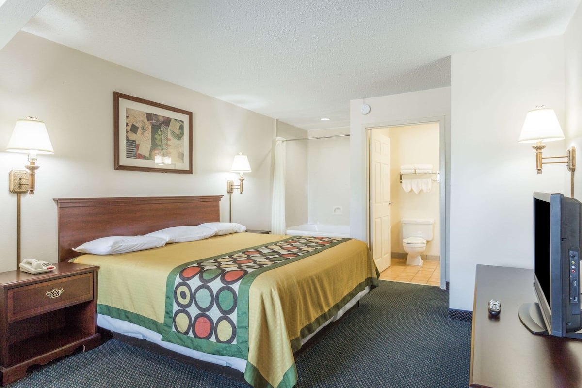 A hotel room with a bed, bedside lamps, a television, and a bathroom visible through an open door.
