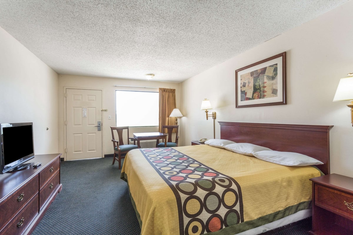 A hotel room with a bed, a desk, a television, and a painting on the wall.