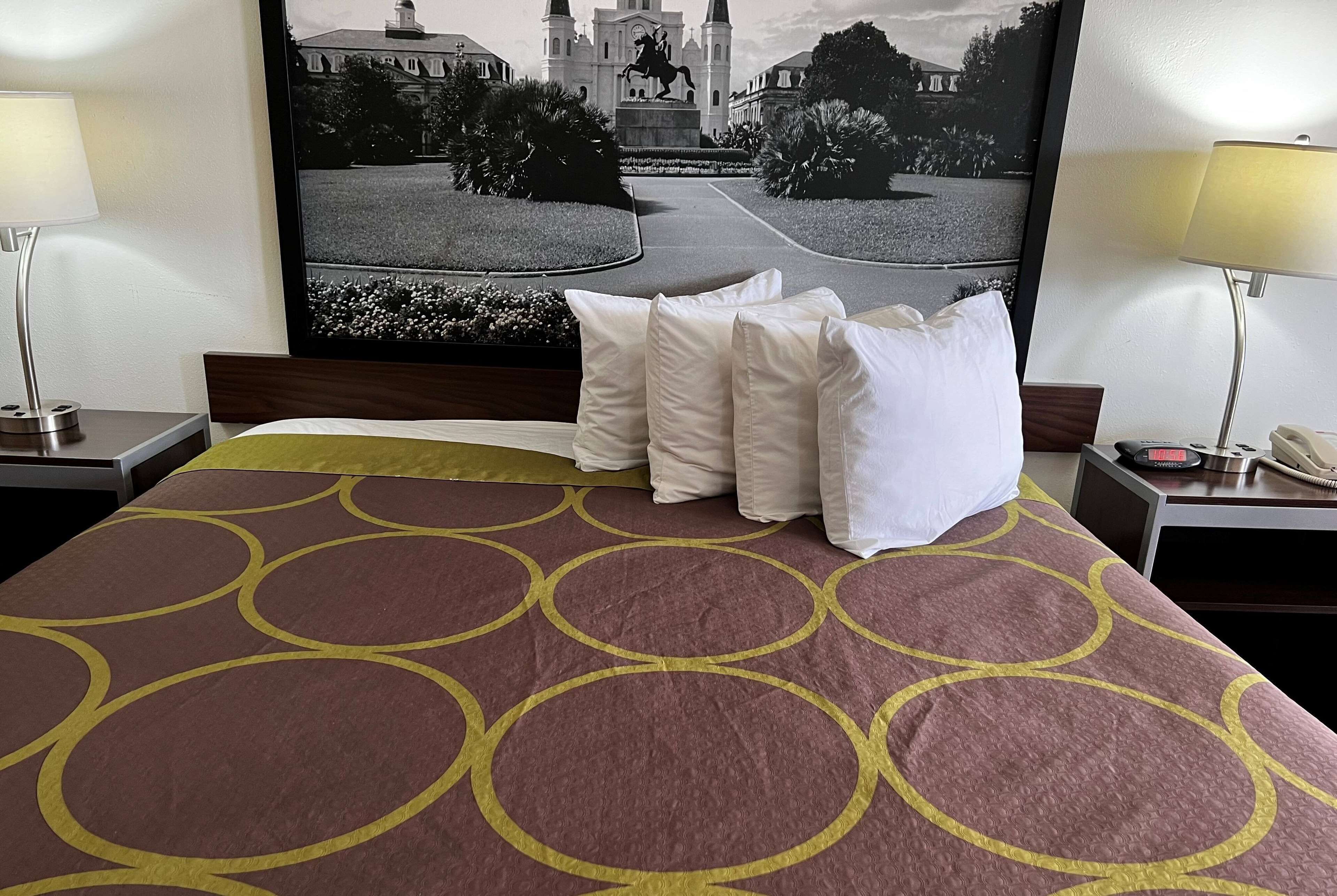 A hotel room with a large bed, a headboard with a mounted picture, two bedside tables with lamps, and a large framed picture on the wall.