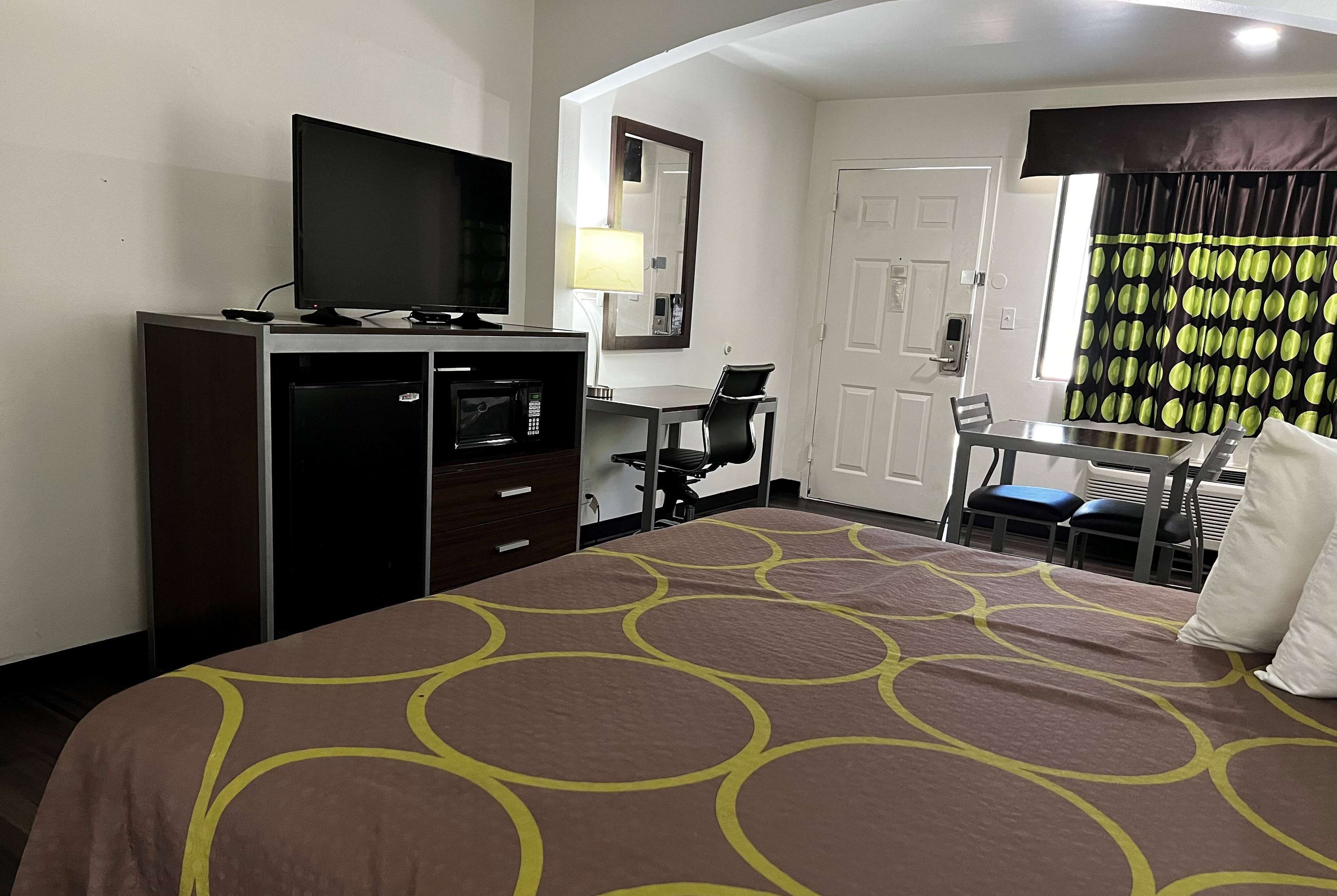 Une chambre d’hôtel avec un lit, un bureau, une chaise, une télévision, un miroir et une porte.