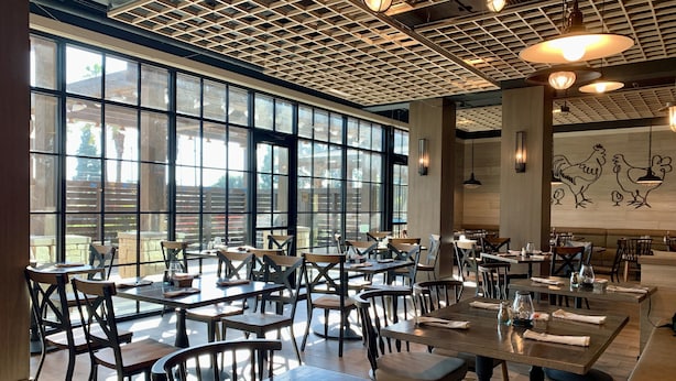 A restaurant with large windows, wooden tables, and chairs. - Knott's Hotel (Buena Park)