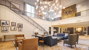 A spacious lobby with a high ceiling, a staircase, and a seating area with sofas and armchairs. - Knott's Hotel (Buena Park)