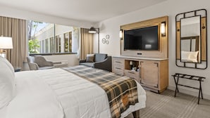 A hotel room with a large bed, a TV, a desk, and a window with curtains. - Knott's Hotel (Buena Park)